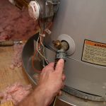 Hand adjusting a valve on a water heater with a warning label, showcasing Maxwell-White Plumbing maintenance techniques.