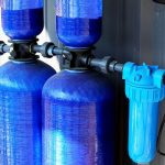 Blue water filtration tanks with black piping and an inline filter unit for plumbing efficiency by Maxwell-White Plumbing.