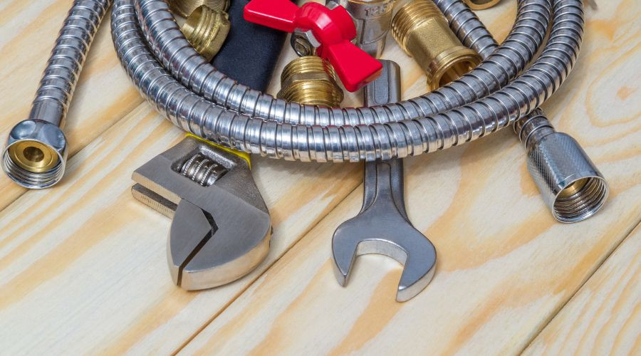 Tools and hoses for plumbing maintenance, featuring wrenches and pipe fittings. Maxwell-White Plumbing prepares for repairs.