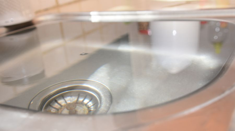 Basin sink with reflective water and drain, surrounding kitchen items, representing Maxwell-White Plumbing services.