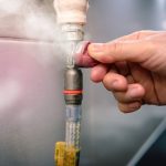 Hand tightening a gas line fitting with visible steam, emphasizing gas leak detection and safety protocols.