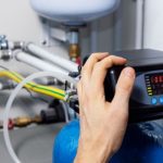 Hand adjusting a water filtration system control panel, showcasing plumbing integration and service access for whole-house water filtration solutions.